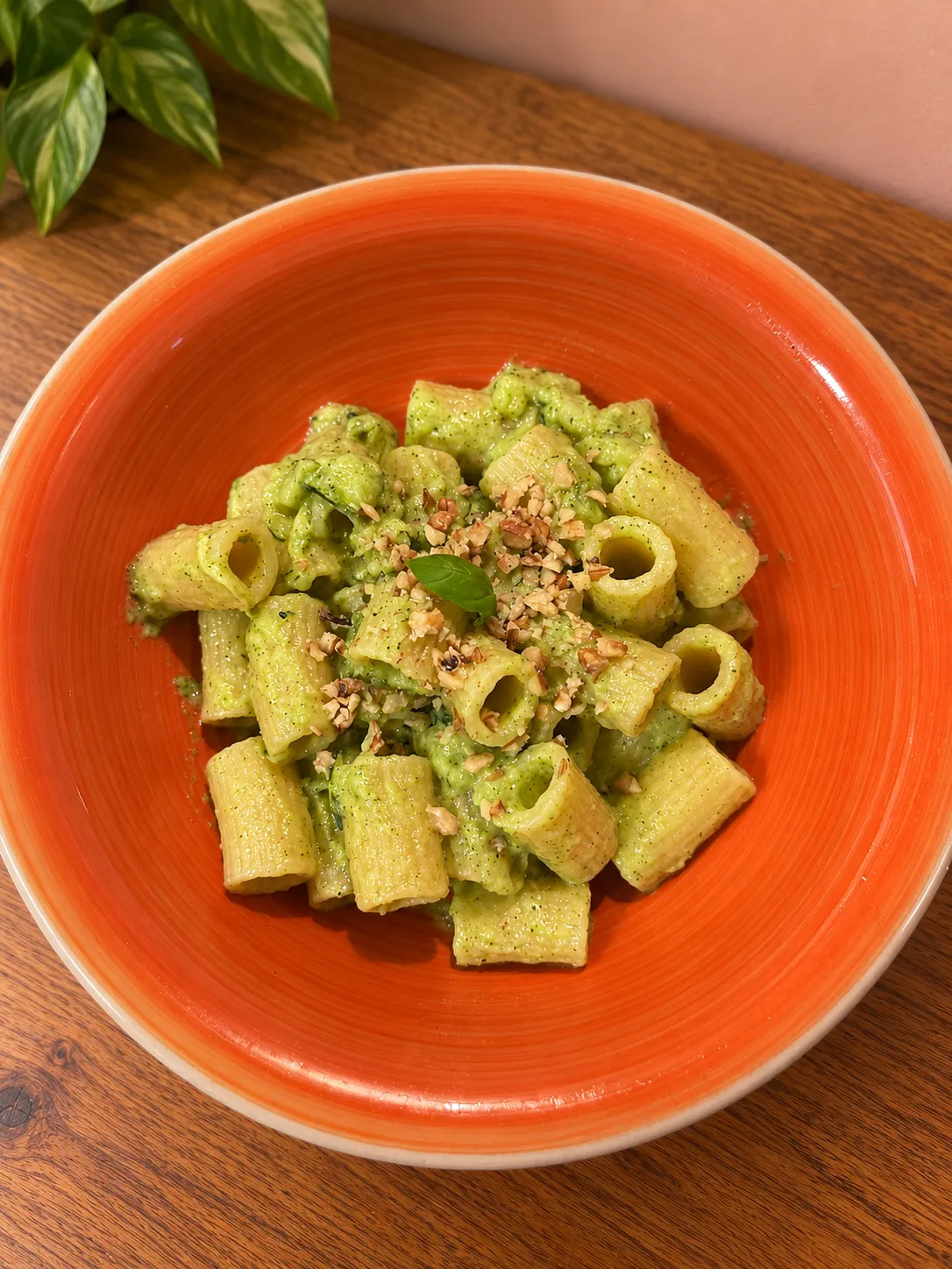 Pasta corta con crema di zucchine e basilico e granella di noci, in un piatto arancione
